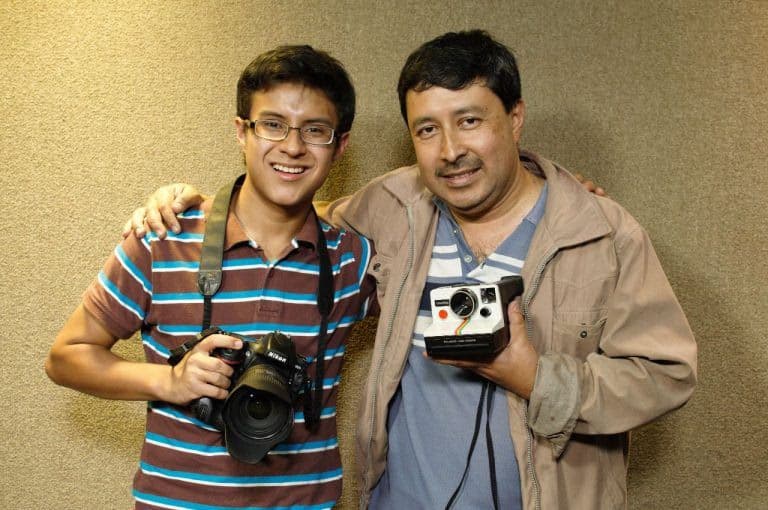 Two photographers smile while holding vintage cameras.