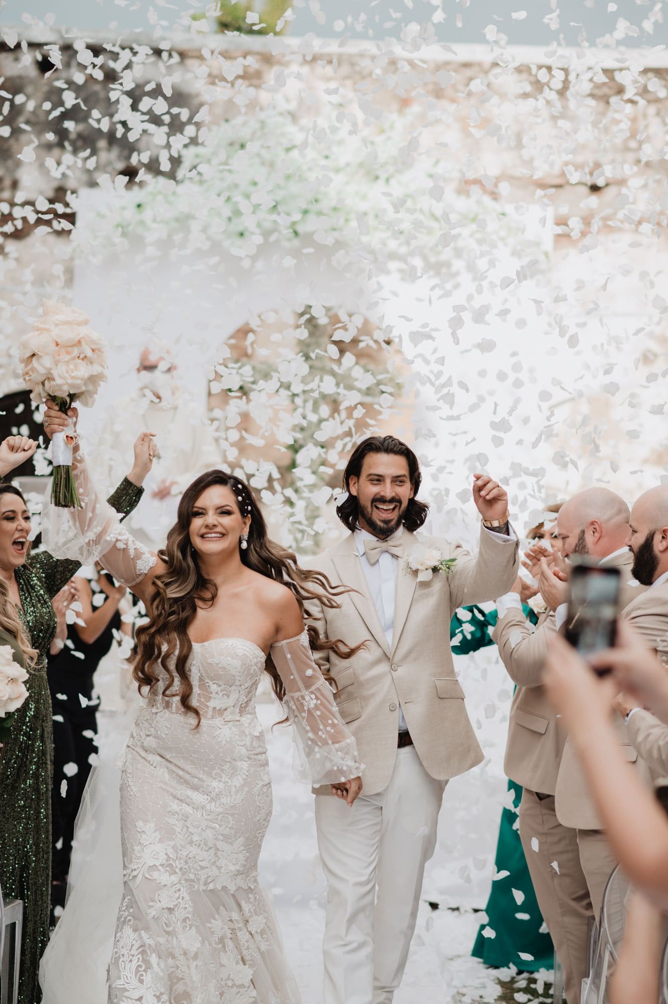 Bride and groom laugh together as guests throw white petal confetti during the joyful recessional in colonial Antigua.