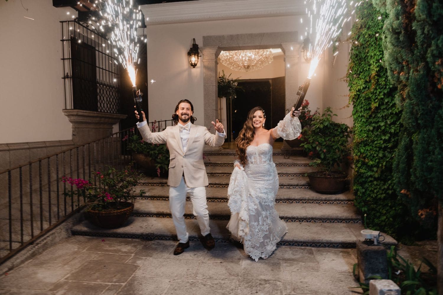 Newlyweds descend a tiled staircase holding sparkler torches as fireworks shoot up beside them at Hotel Pensativo.