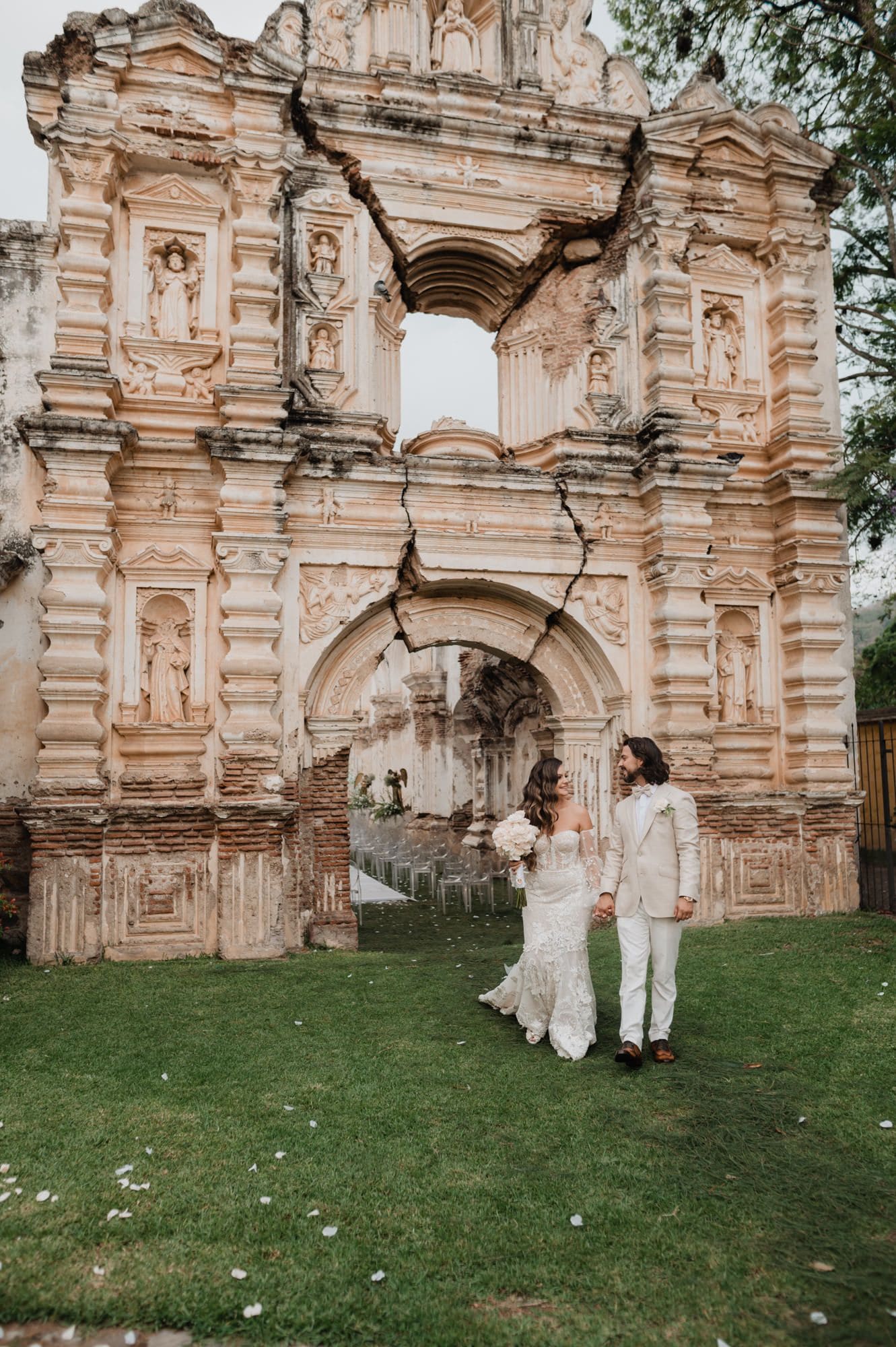 Couple walks hand-in-hand past the carved baroque facade of La Antigua's ruined church on their wedding day.