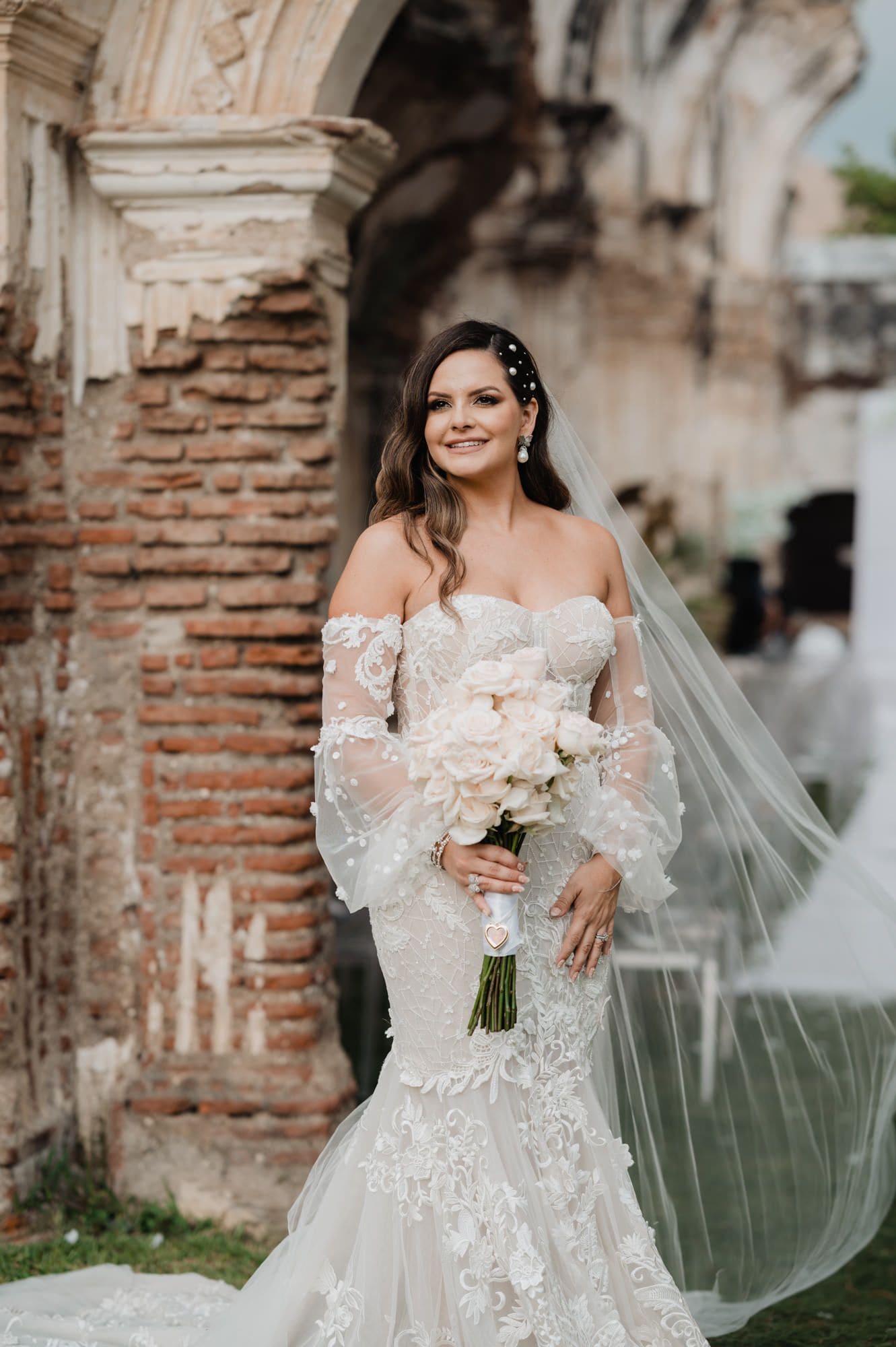 Solo bridal portrait of Marite holding a white rose bouquet beside a brick ruin column.