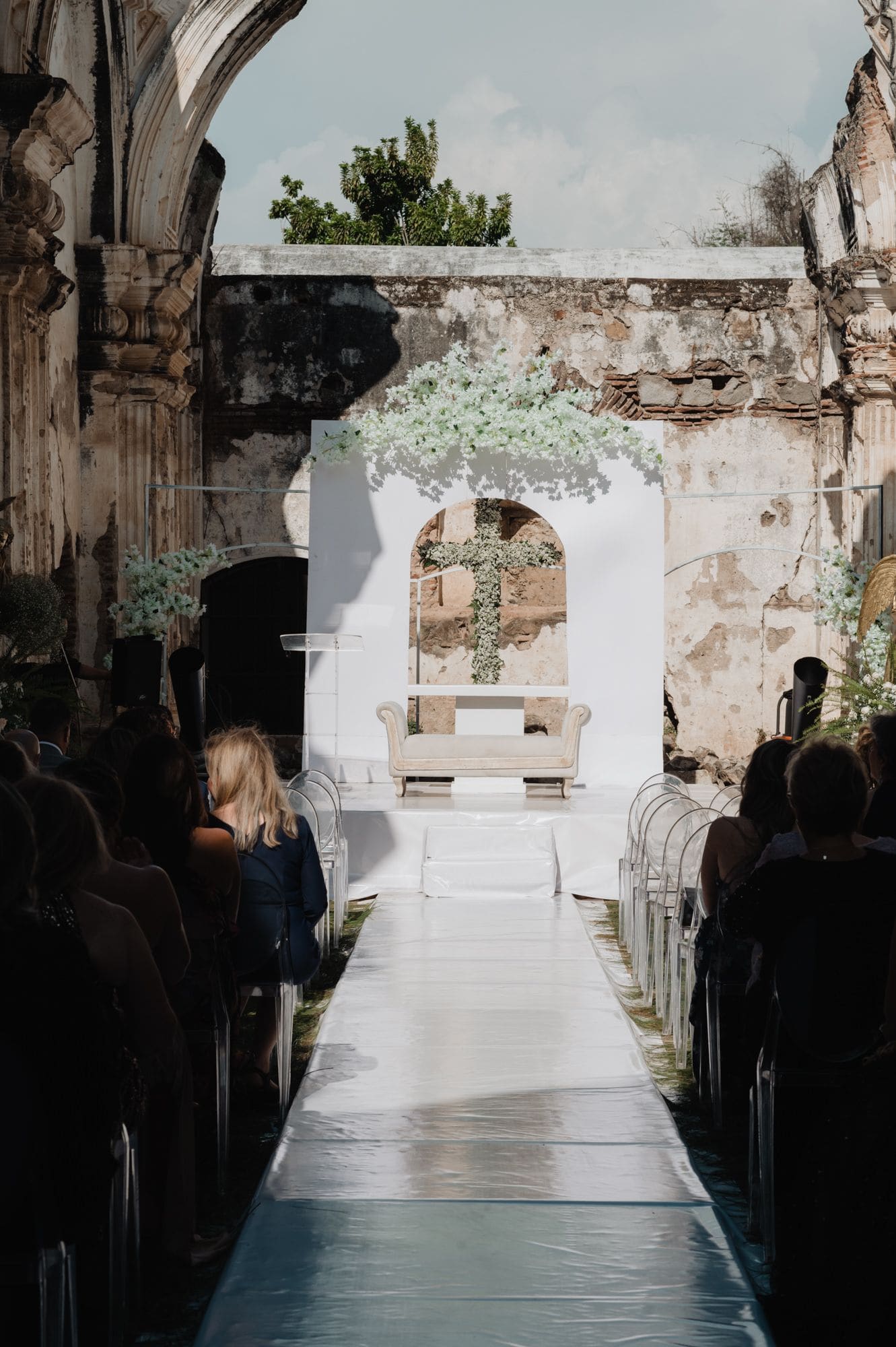 Wide aisle view of the white modern altar with a flower cross under a baby's breath arch inside Casa de la Ruina, Antigua Guatemala.