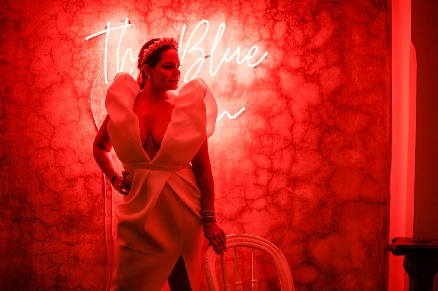 Bride poses solo in her dramatic ruffled second-look dress against a neon-lit wall at the Hotel Pensativo reception.