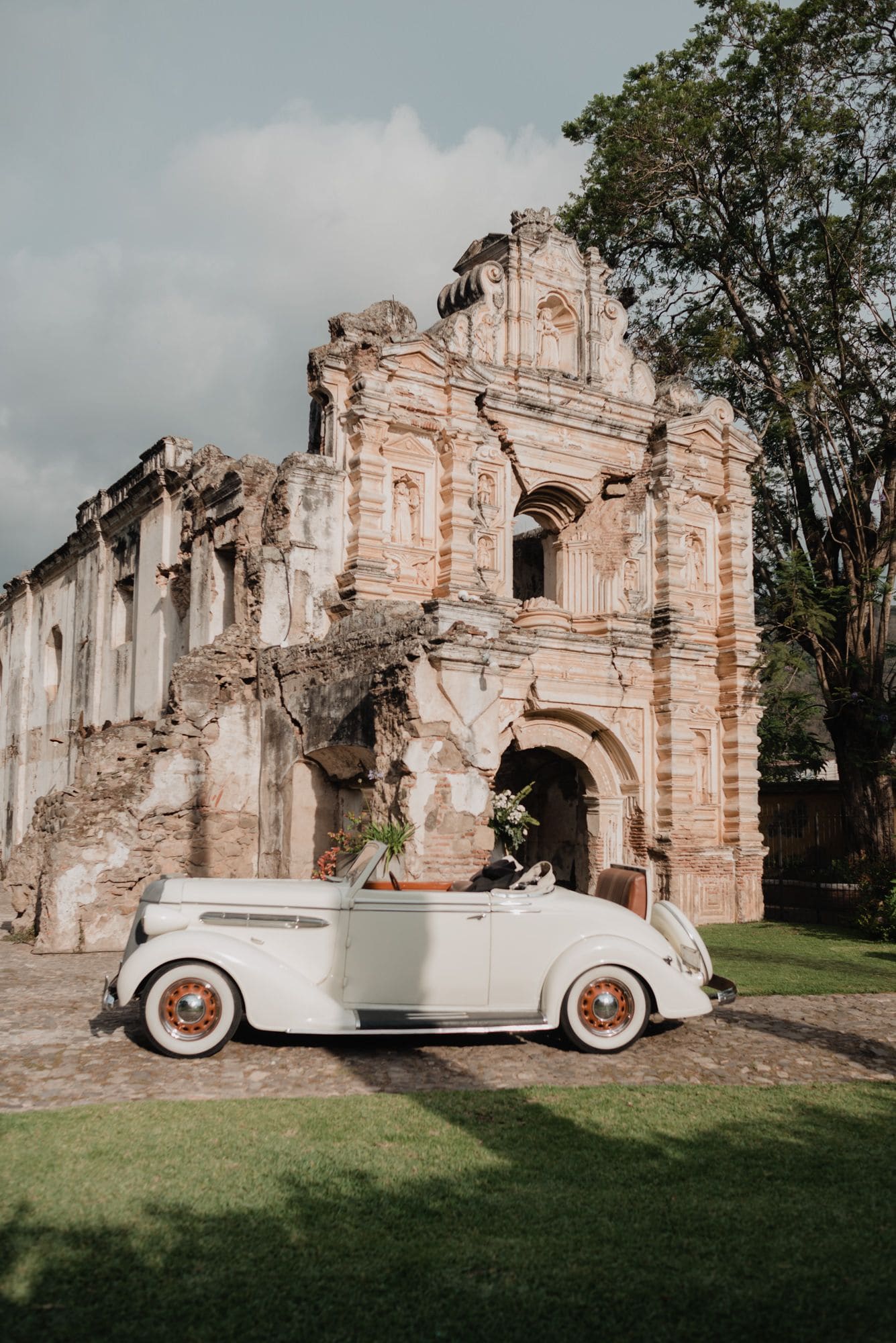 Vintage white convertible parked in front of a carved baroque facade in ruins after the ceremony.