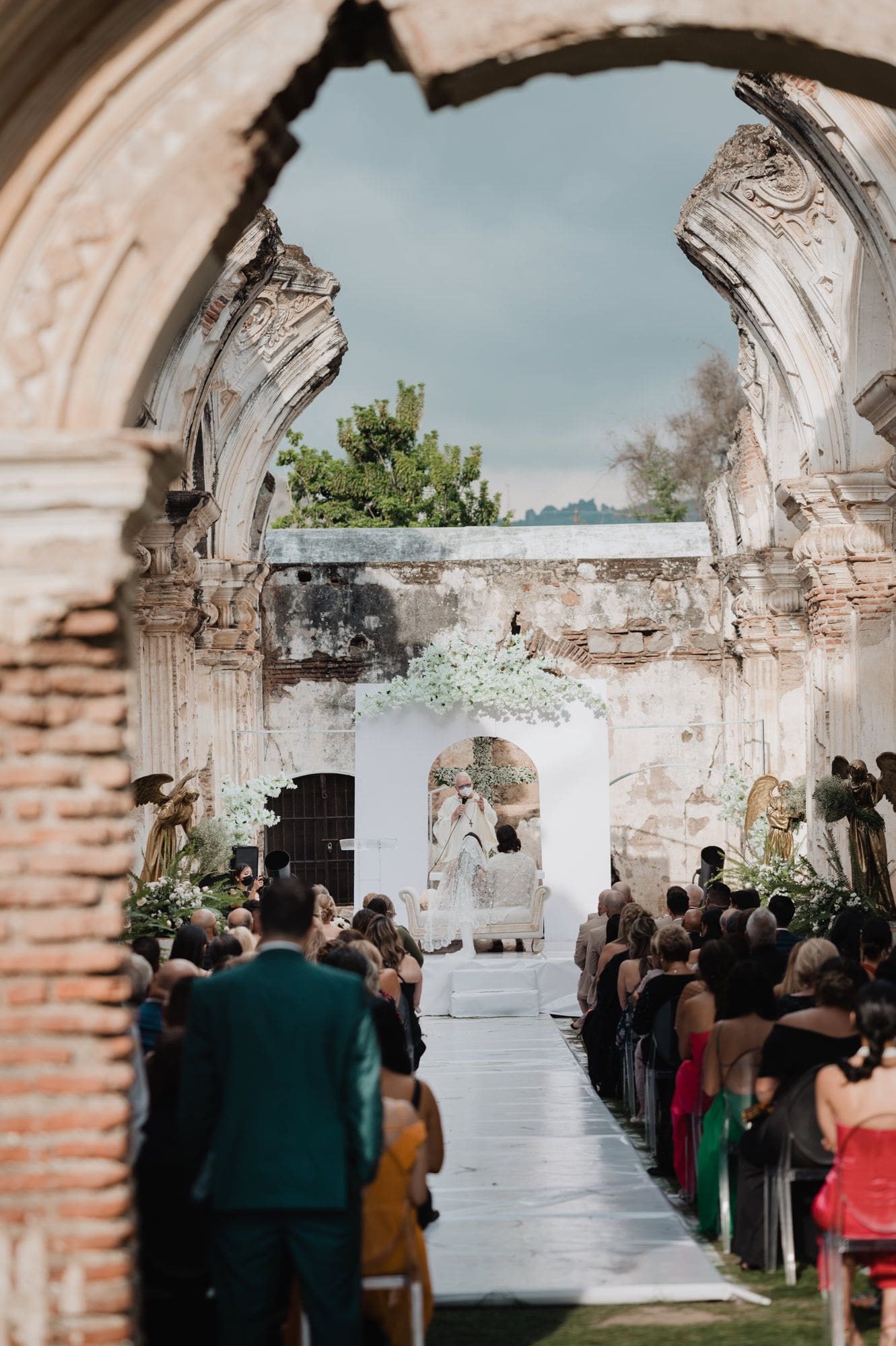 Ceremony viewed through an arched colonial portal with the officiant and altar at the end of the aisle inside Casa de la Ruina.