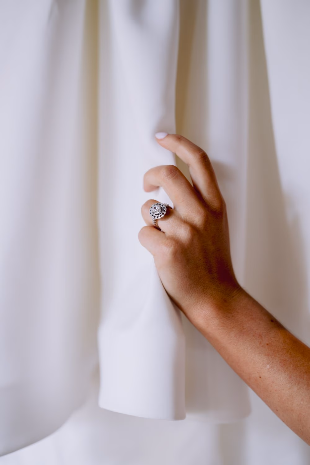 Bride smiles up at her wedding dress hanging from a wooden beam in a colonial getting-ready room with warm exposed-brick ceiling.