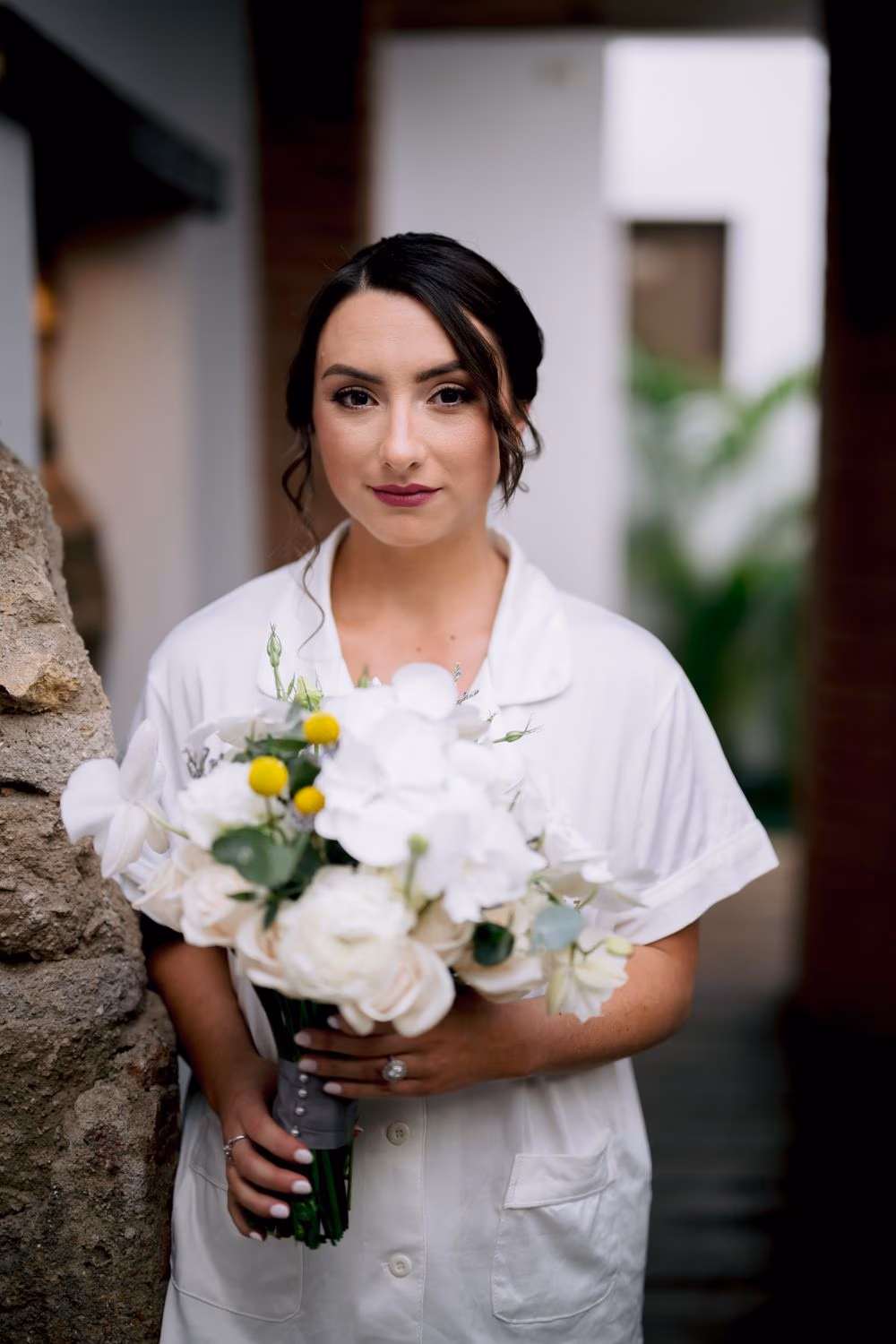 Bridal bouquet of white orchids, roses and craspedia held by the bride, her engagement ring framed against the stems.