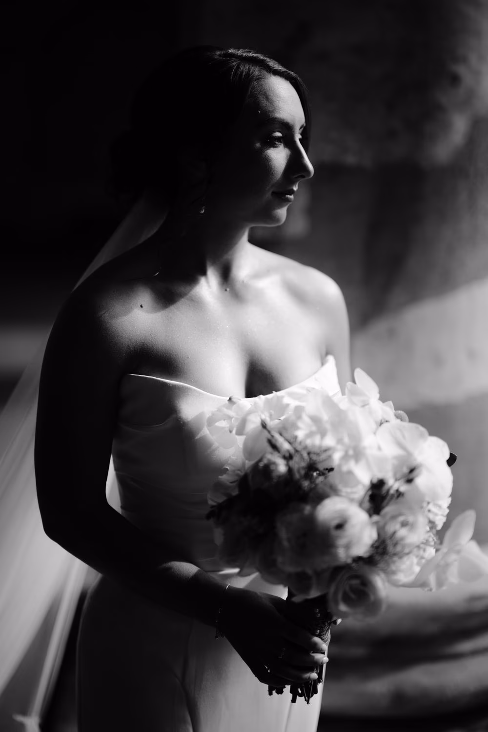 Full bridal portrait — Alexis with her veil, gown and bouquet against a softly textured colonial wall.