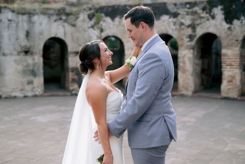 Couple share a smile facing each other inside the convent courtyard, arched stone bays in the background.