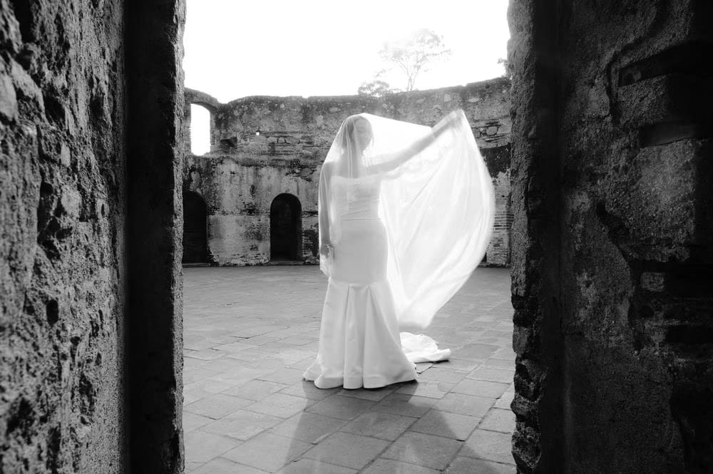 Black-and-white silhouette of the bride spinning her veil in the open courtyard, light pouring in from above.