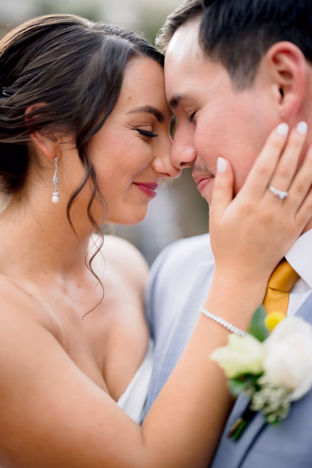 Extreme close-up of bride and groom touching noses, the bride's hand resting on his cheek showing wedding band and engagement ring.