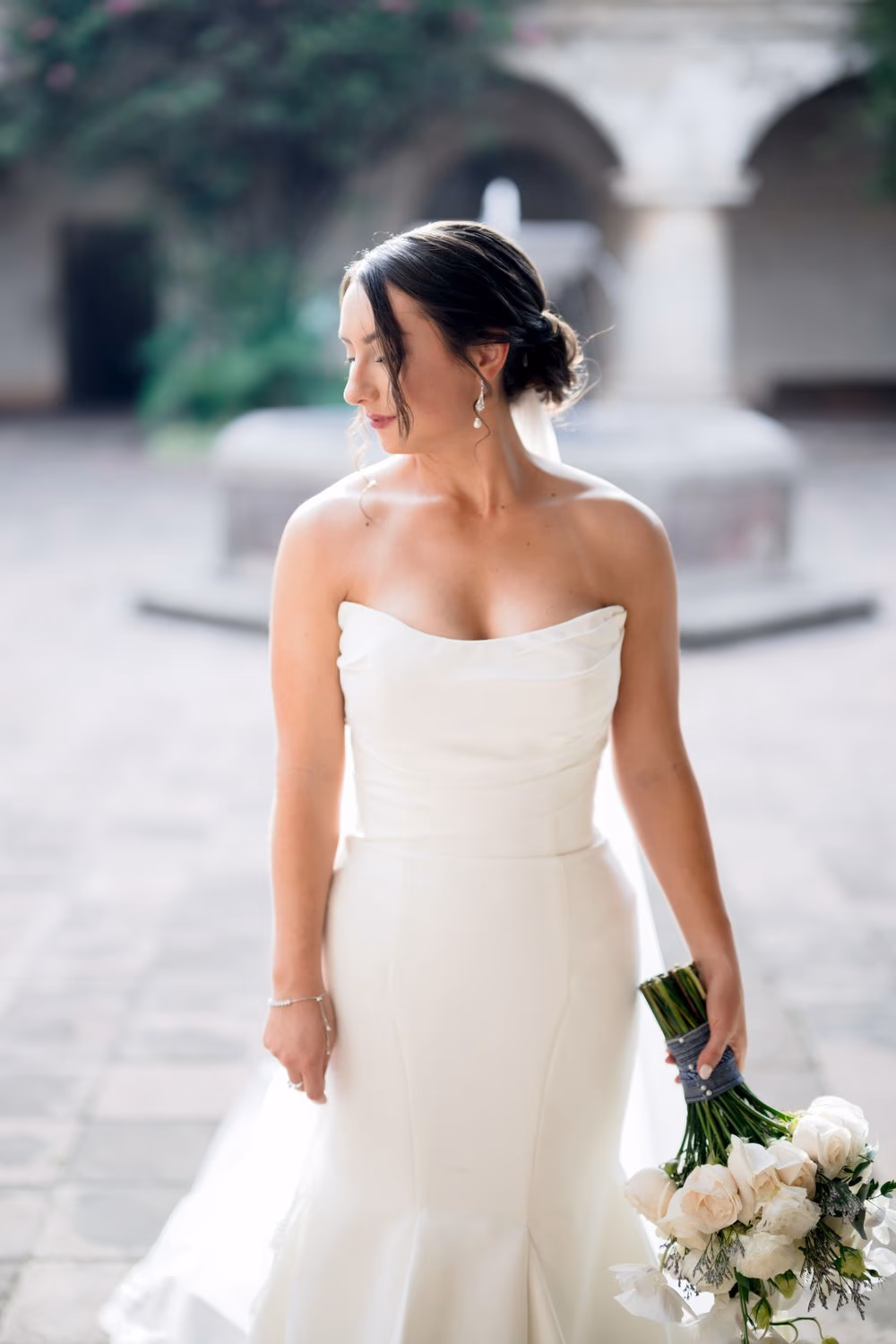 Bridal portrait — Alexis looks down toward her bouquet in the courtyard, hora dorada light softening her silhouette.