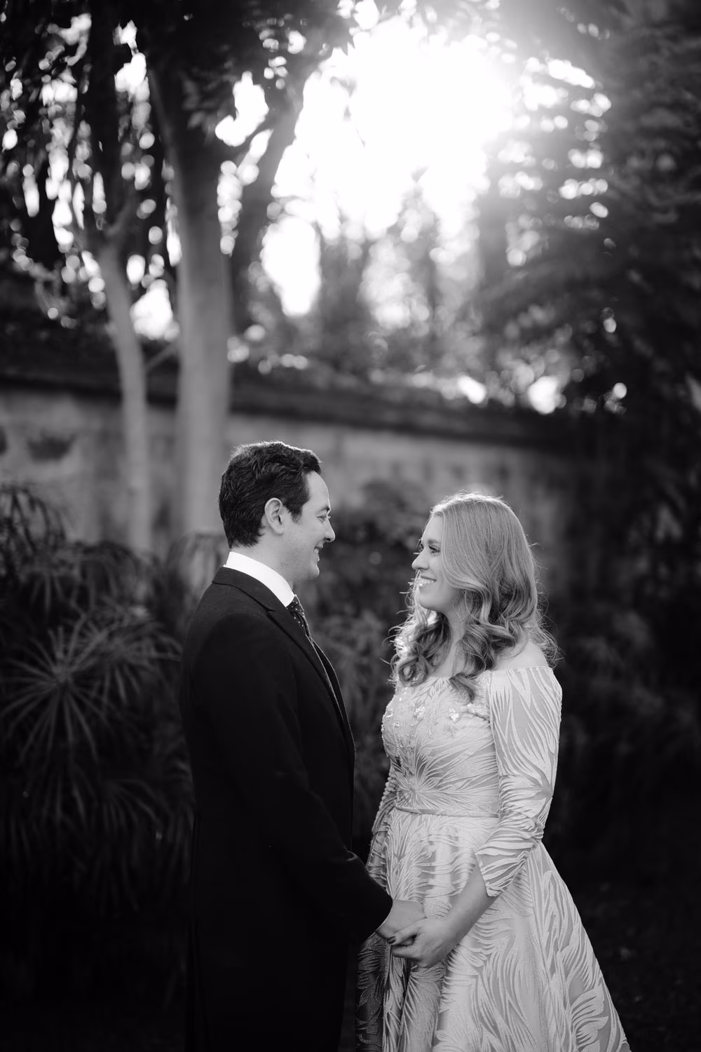 Black-and-white portrait of the bride and groom smiling at each other in a sunlit colonial garden in Antigua Guatemala.