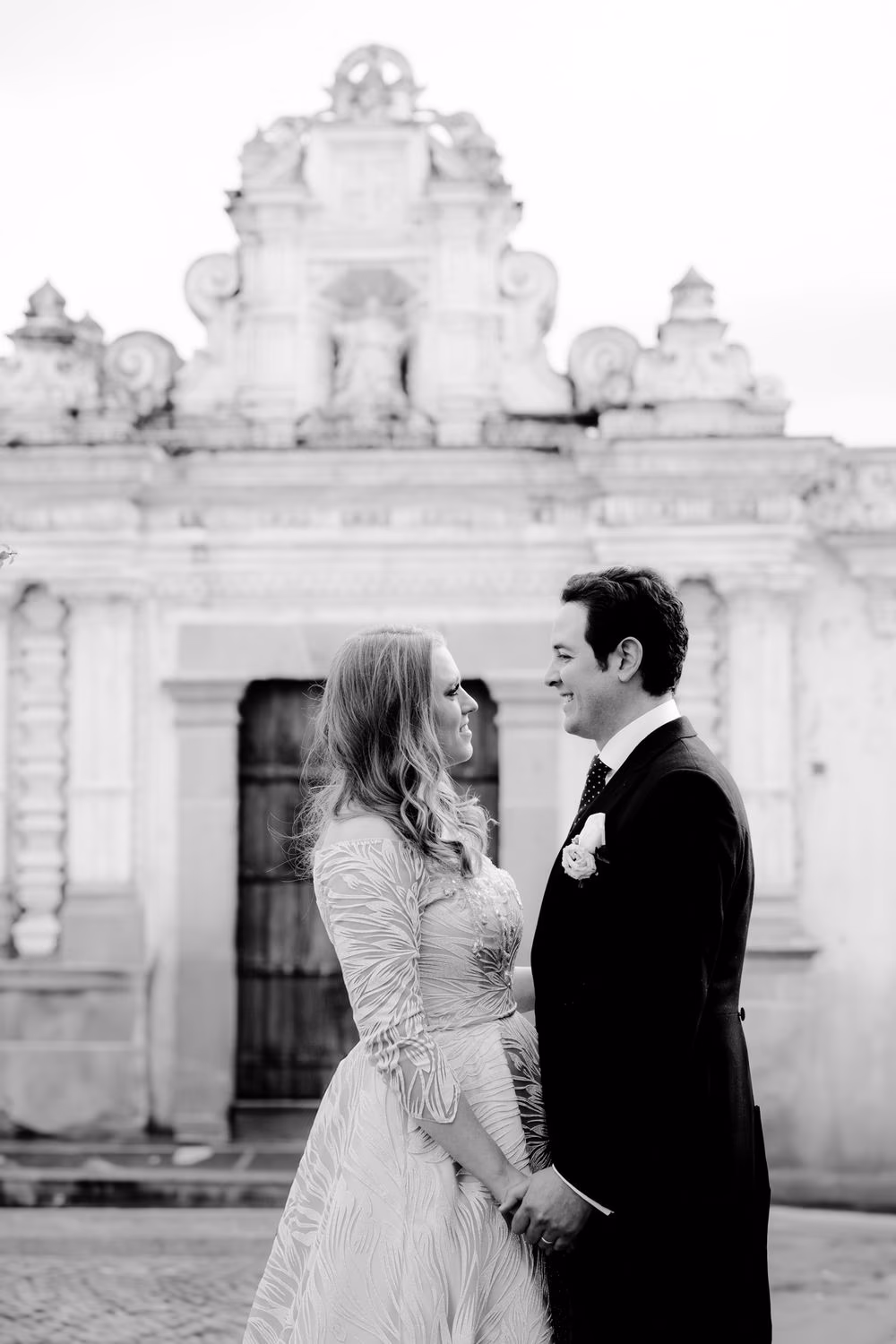 Black-and-white profile portrait of the couple holding hands in front of an ornate colonial facade in La Antigua.