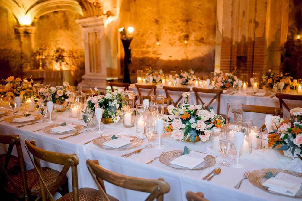 Long reception table aligned with the ruined arches, warm uplighting on weathered walls — colonial ruins wedding in Antigua.