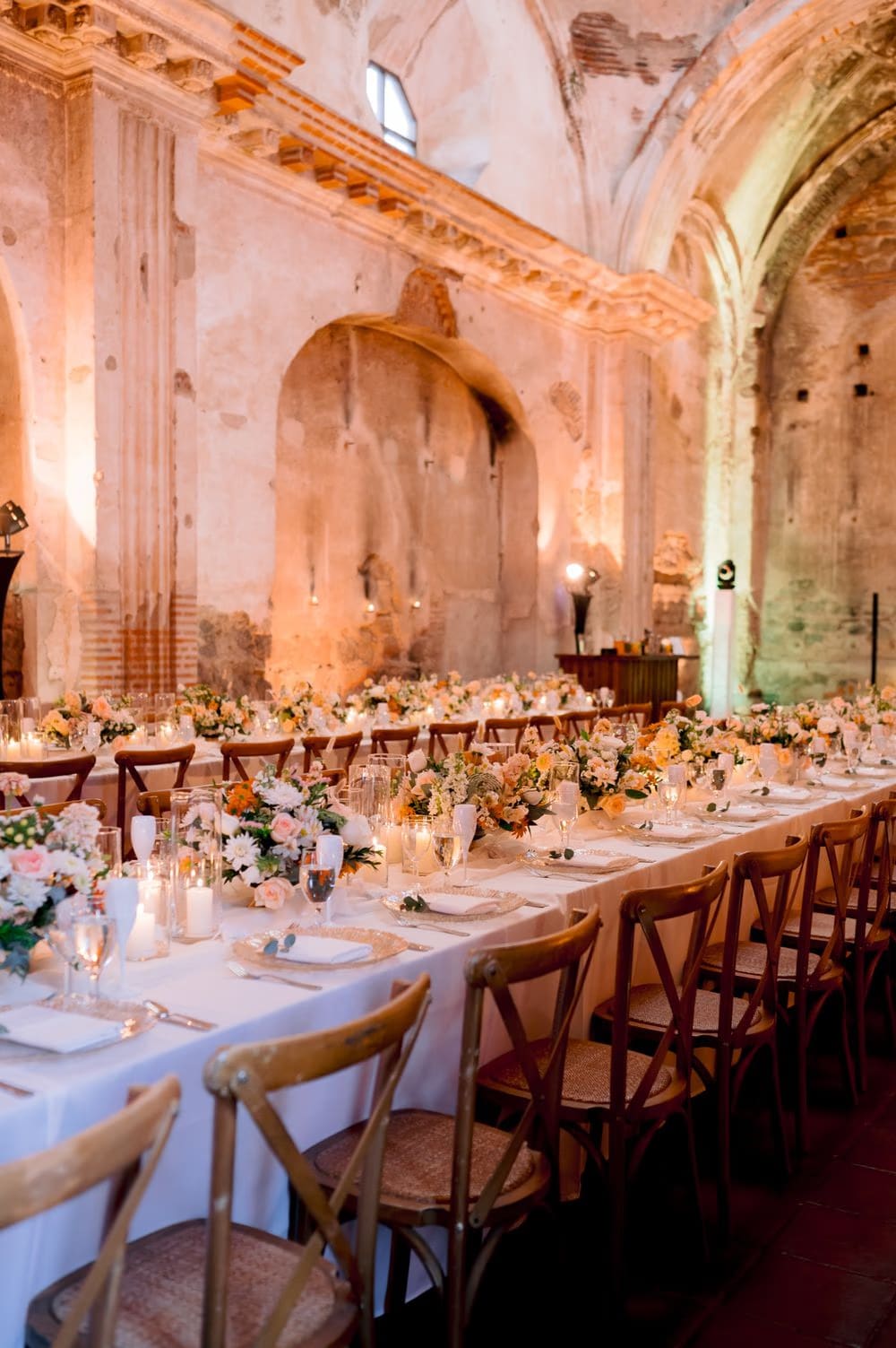 Black-and-white portrait of the bride and groom standing in the candle-lit nave of San José el Viejo Ruins with the long reception table behind them.