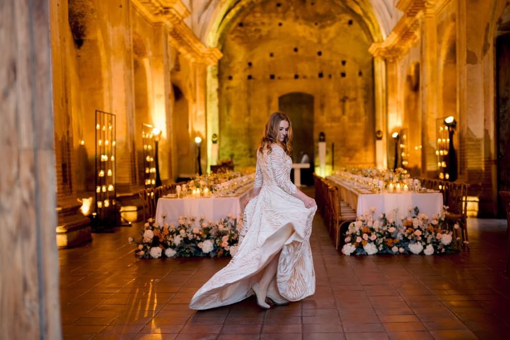 Bride twirls her embroidered gown between two glowing banquet tables in the warmly lit ruins — intimate wedding in Antigua.