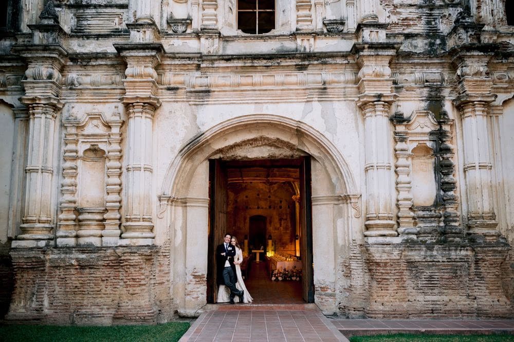 Tiny silhouette of the couple framed inside the towering carved archway of the ruins, glowing reception behind them — destination wedding in Antigua.