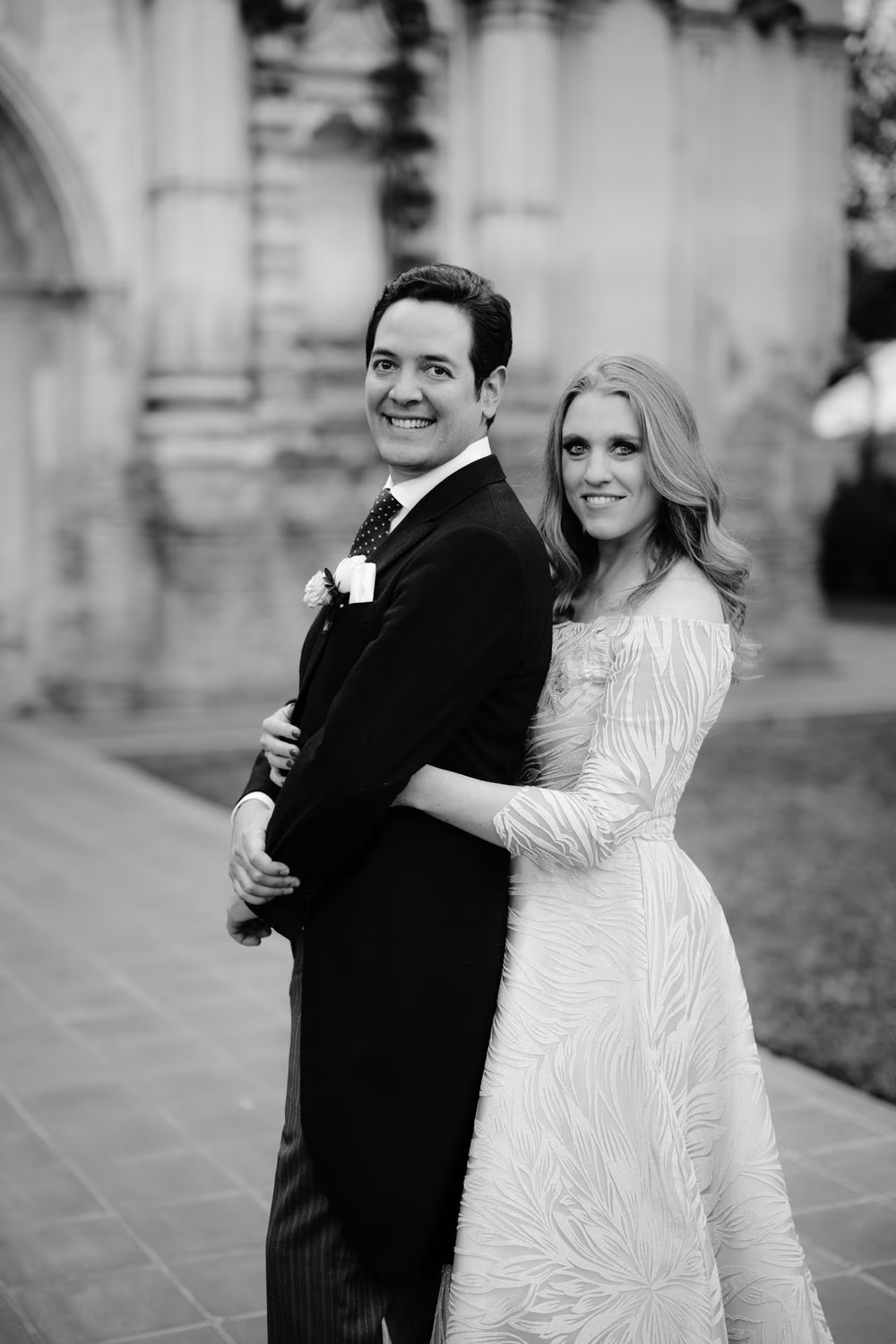 Black-and-white version of the bride embracing the groom from behind in front of the ruins facade in Antigua.