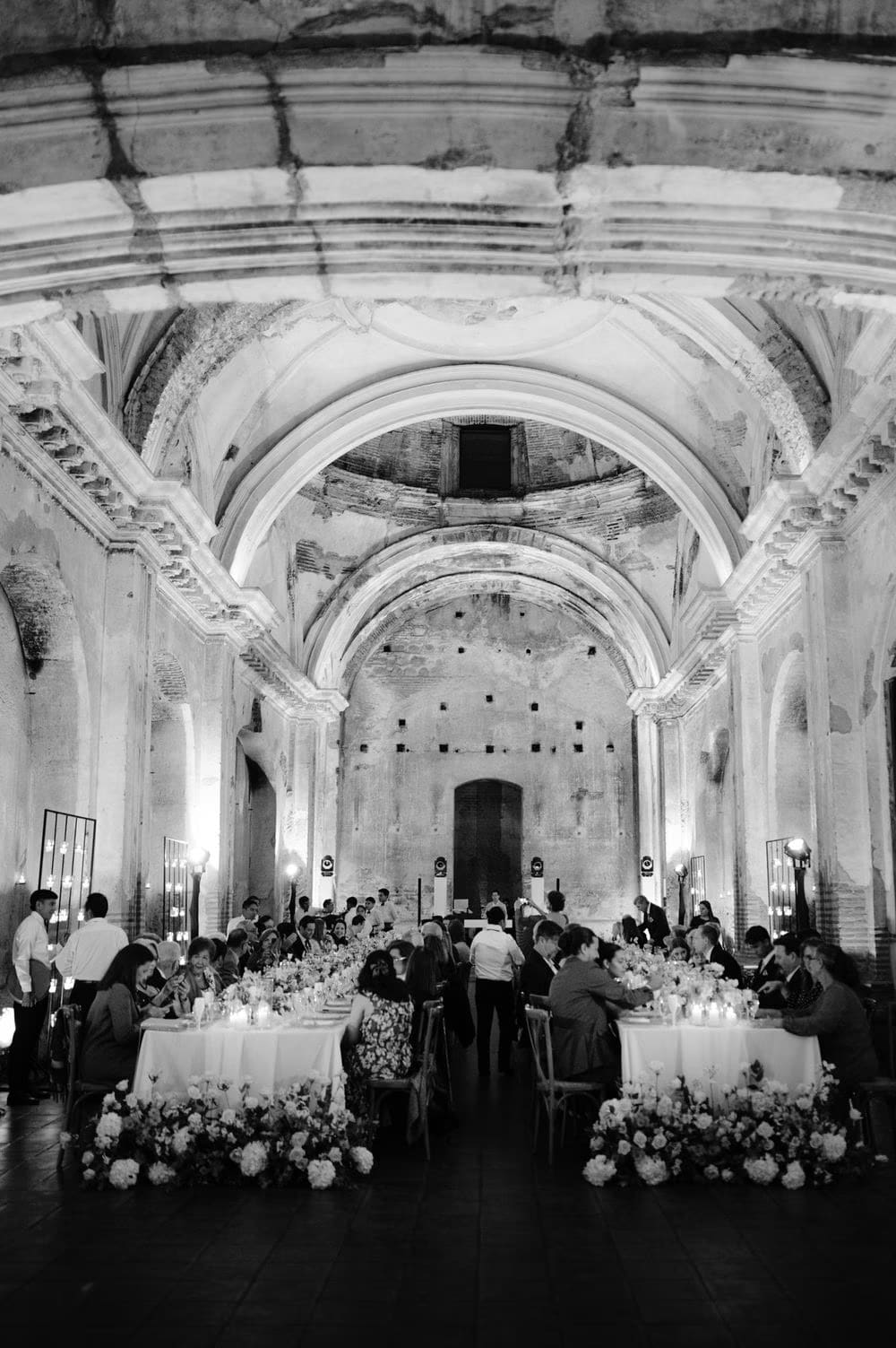 Black-and-white wide shot of guests seated under the towering vaulted ceiling during the wedding reception in Antigua Guatemala.