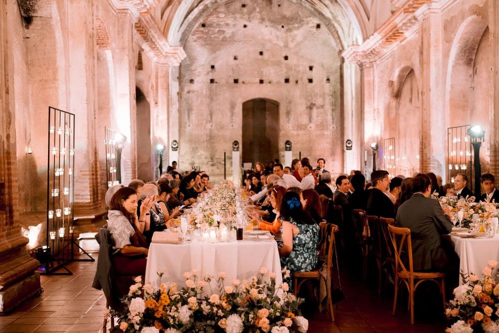 Guests gather around the long table during dinner — catering by Casa Troccoli inside the candle-lit ruins in colonial Antigua.