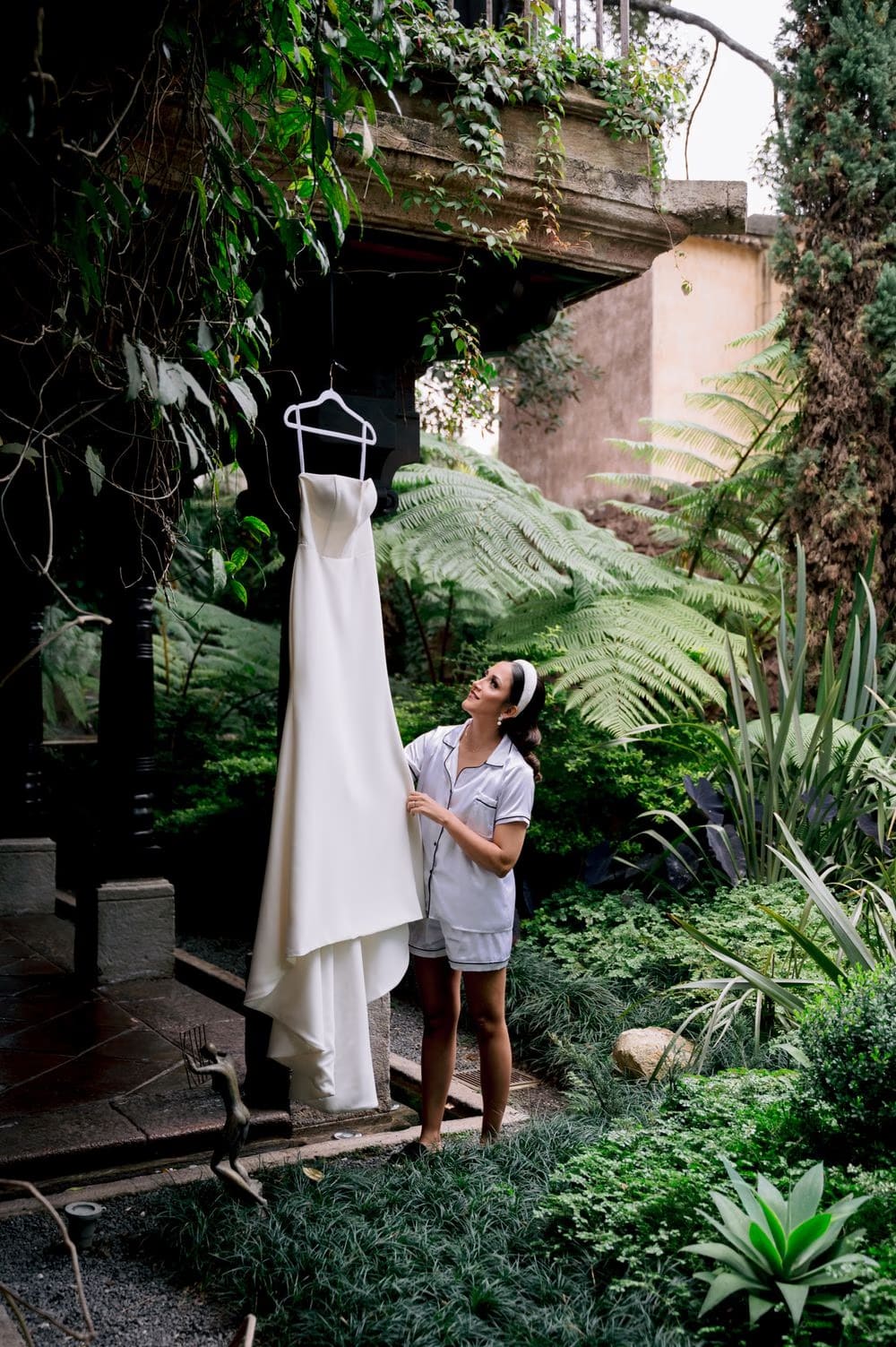 Bride admires her wedding dress hanging in a lush tropical courtyard at El Convento Boutique Hotel.