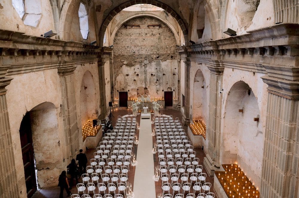 Wide aerial view of Capuchinas Ruins set with rows of chairs and tapered candles for the wedding ceremony in Antigua Guatemala.
