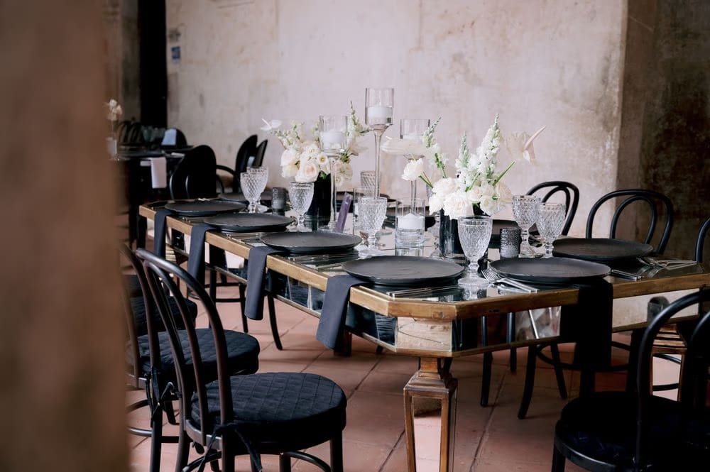 Reception table set with black plates, smoked glassware and white florals at a Capuchinas Ruins wedding.