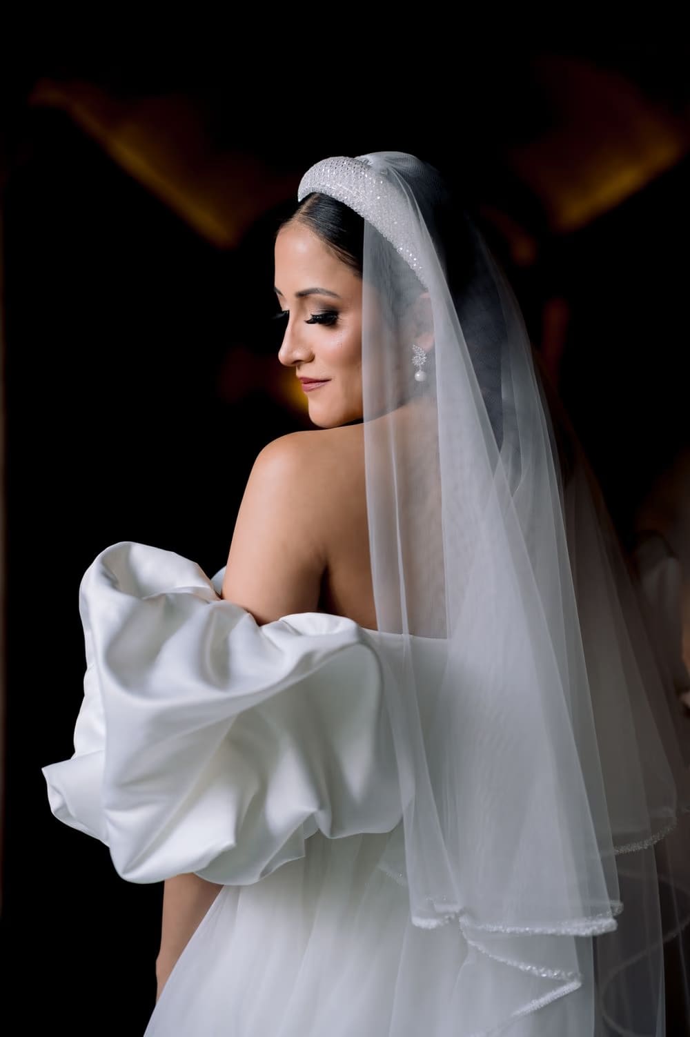 Bride photographed from behind with veil and beaded headband — candle-lit black-and-white editorial portrait.