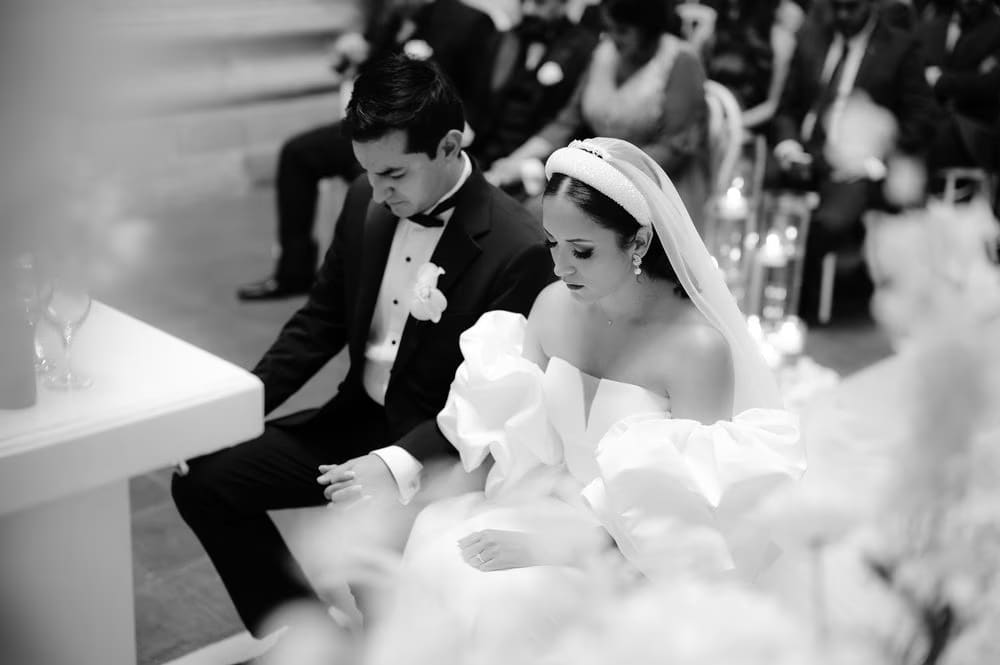 Bride and groom seated and bow their heads in prayer during the wedding ceremony — black-and-white candid.