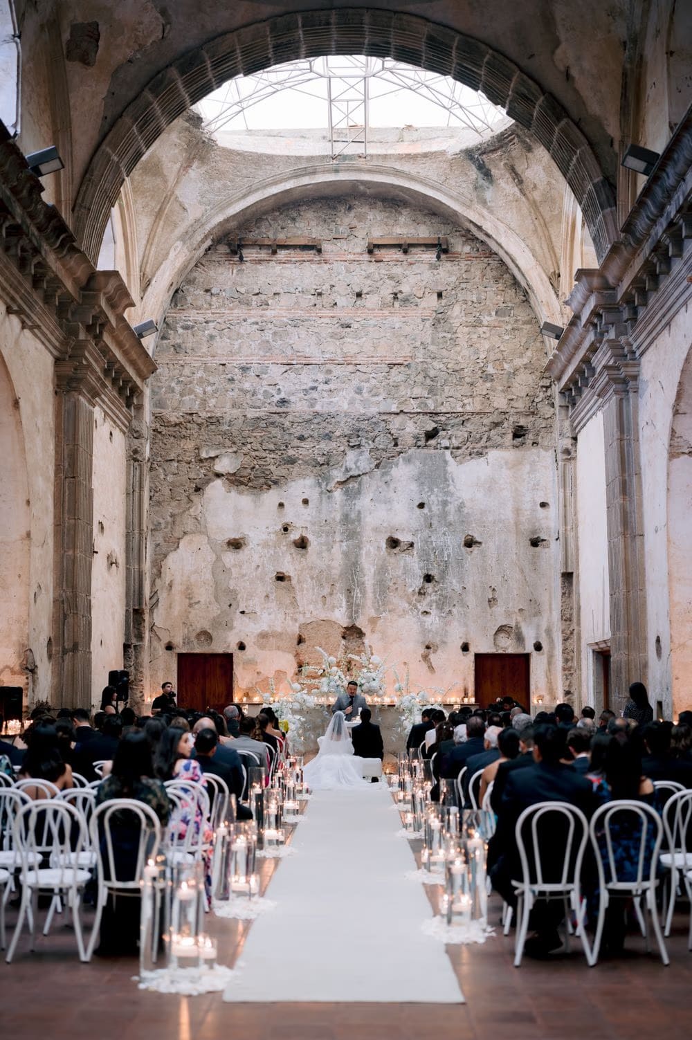 Symmetrical view down the candle-lit aisle of the convent ruins toward the floral altar during the ceremony.