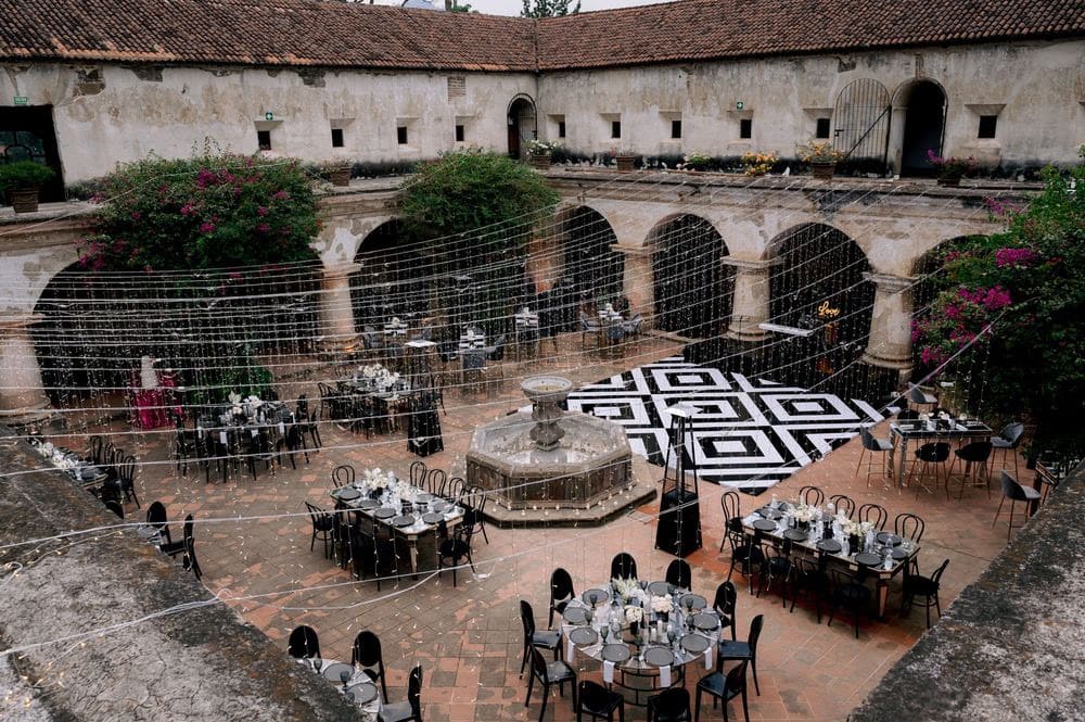Reception courtyard with black-and-white geometric dance floor, central fountain and tables ringing the cloister.