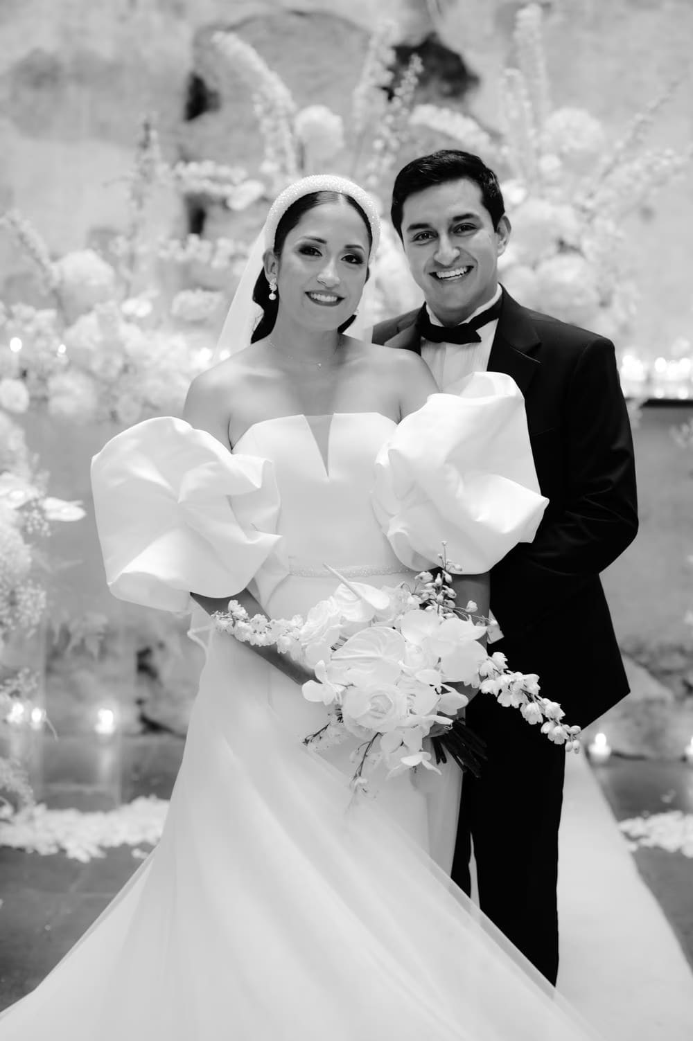 Black-and-white formal portrait of the bride and groom with a cascading orchid bouquet and floral installation behind.