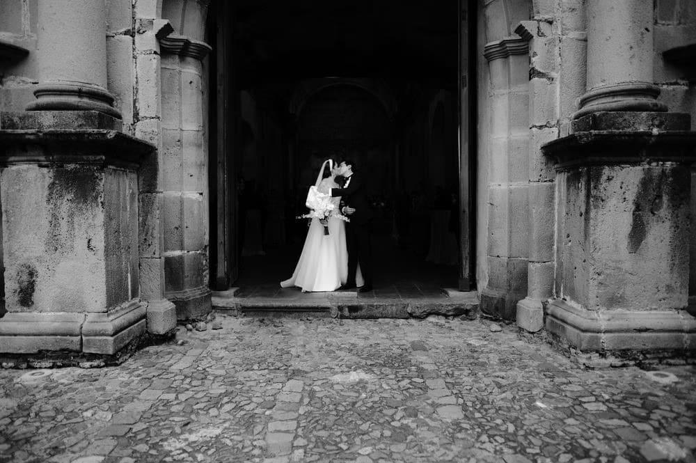 Couple silhouette inside the colonial doorway of the convent, framed by massive stone pillars on a cobblestone street.