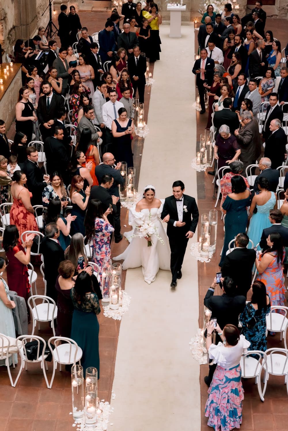 Overhead view of Andrea and Josue walking the aisle as guests applaud and capture the recessional on their phones.