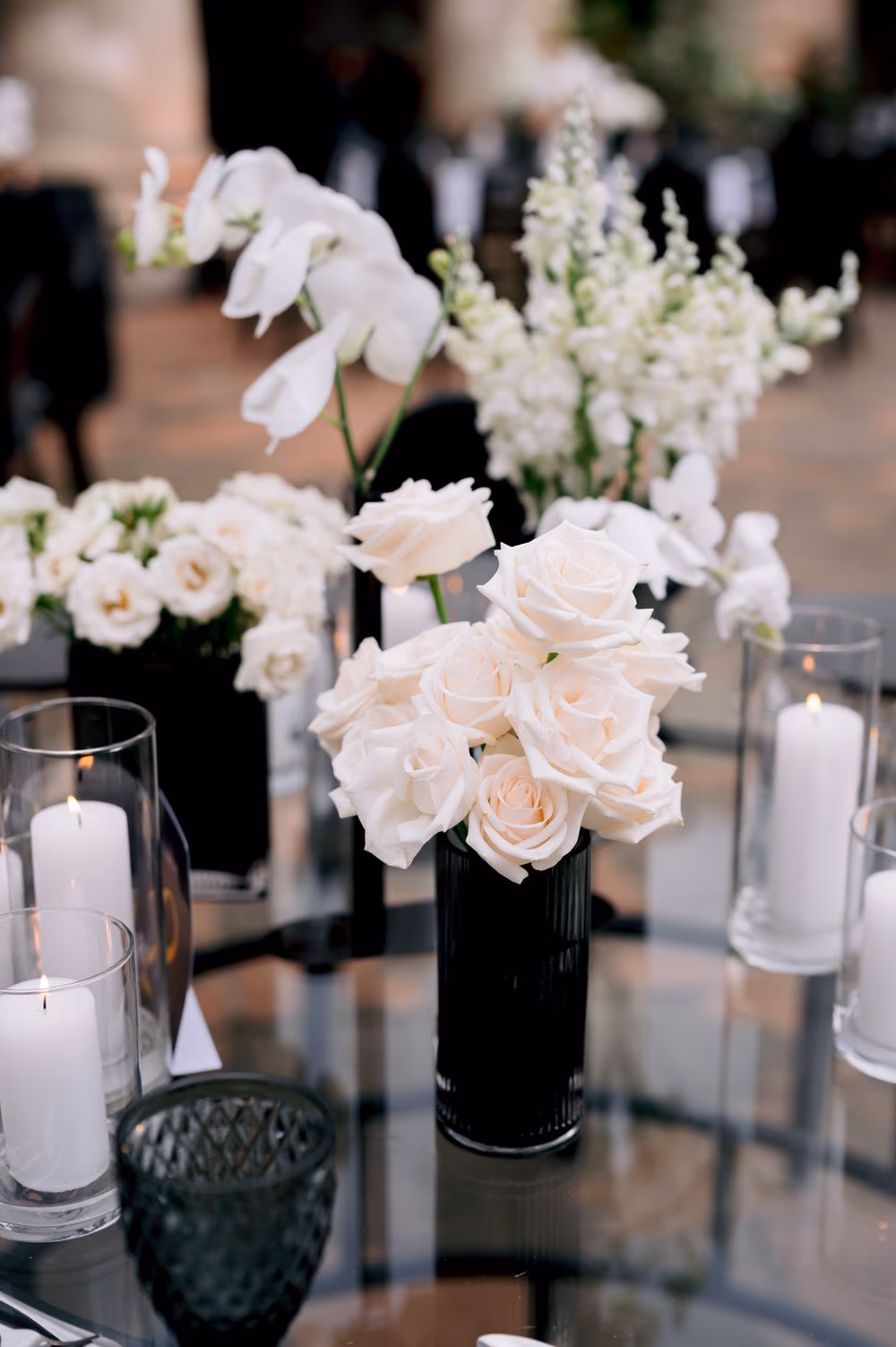 Centerpiece detail — cream roses, orchids and snapdragons in a black ribbed vase among pillar candles.