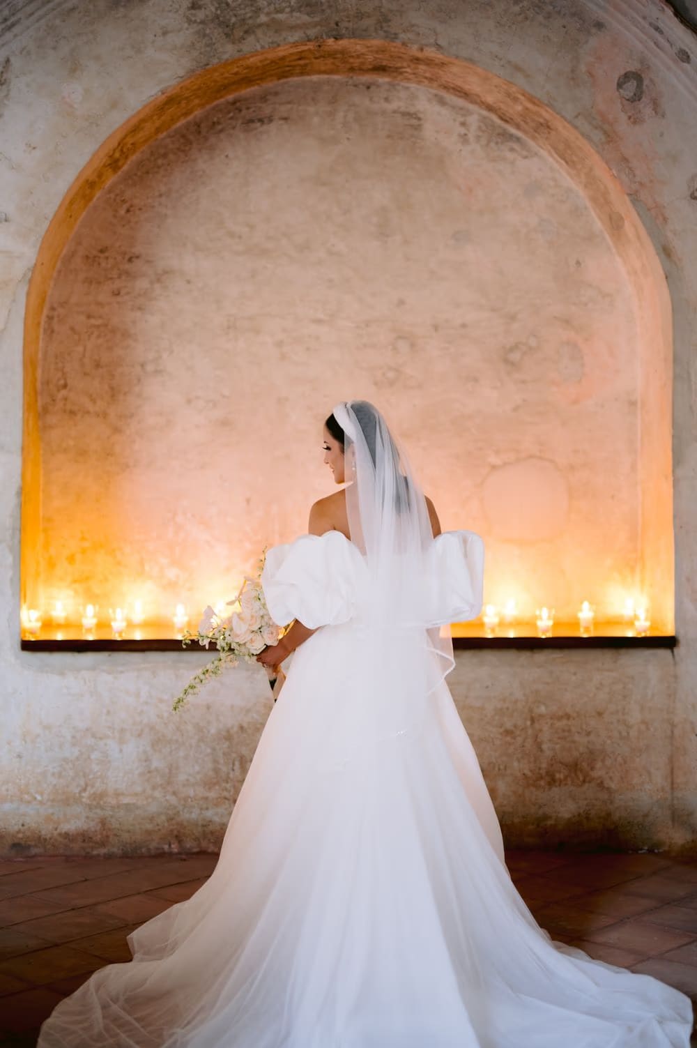 Bride photographed from behind in a glowing arched alcove lined with candles inside the convent ruins.
