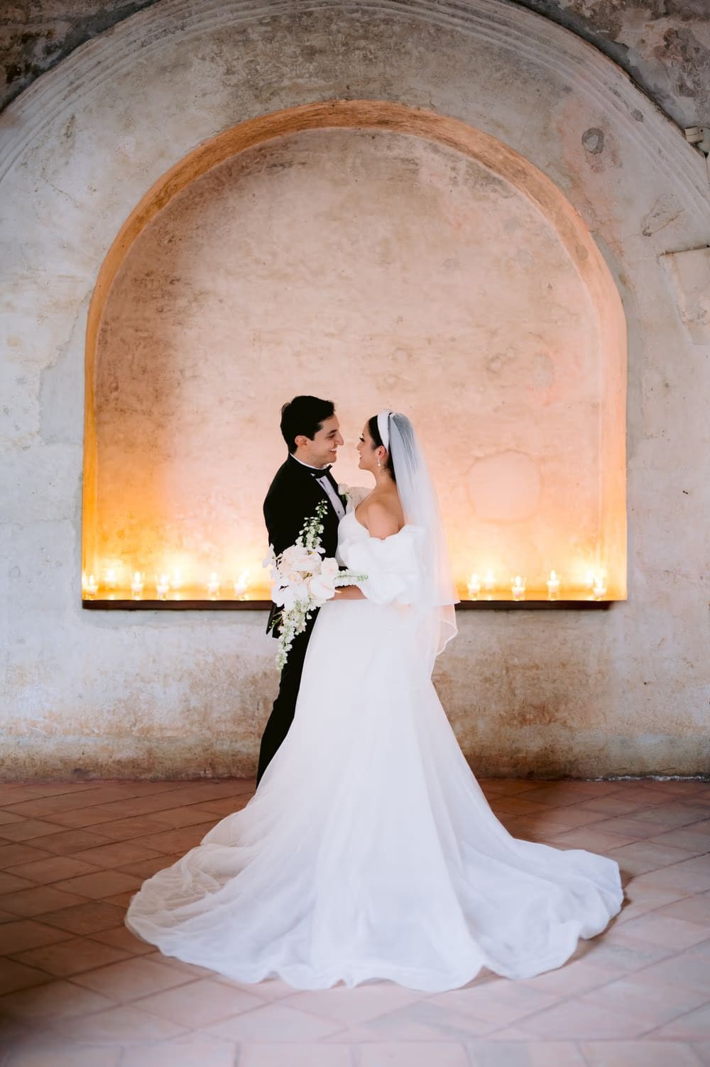 Bride and groom face each other in a candle-lit arch — intimate couple portrait at the convent ruins.