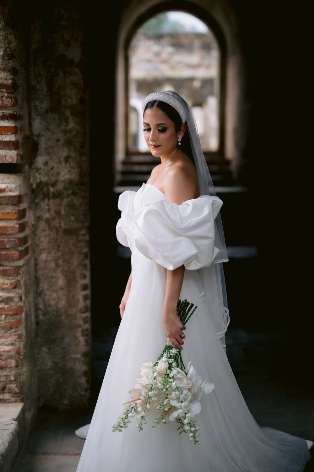 Bride pauses in a brick-framed corridor of the convent ruins holding her bouquet — Antigua Guatemala destination wedding.