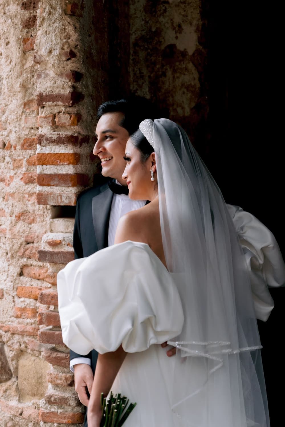 Couple looks off into the distance from a stone arch in colonial Antigua — editorial wedding portrait.