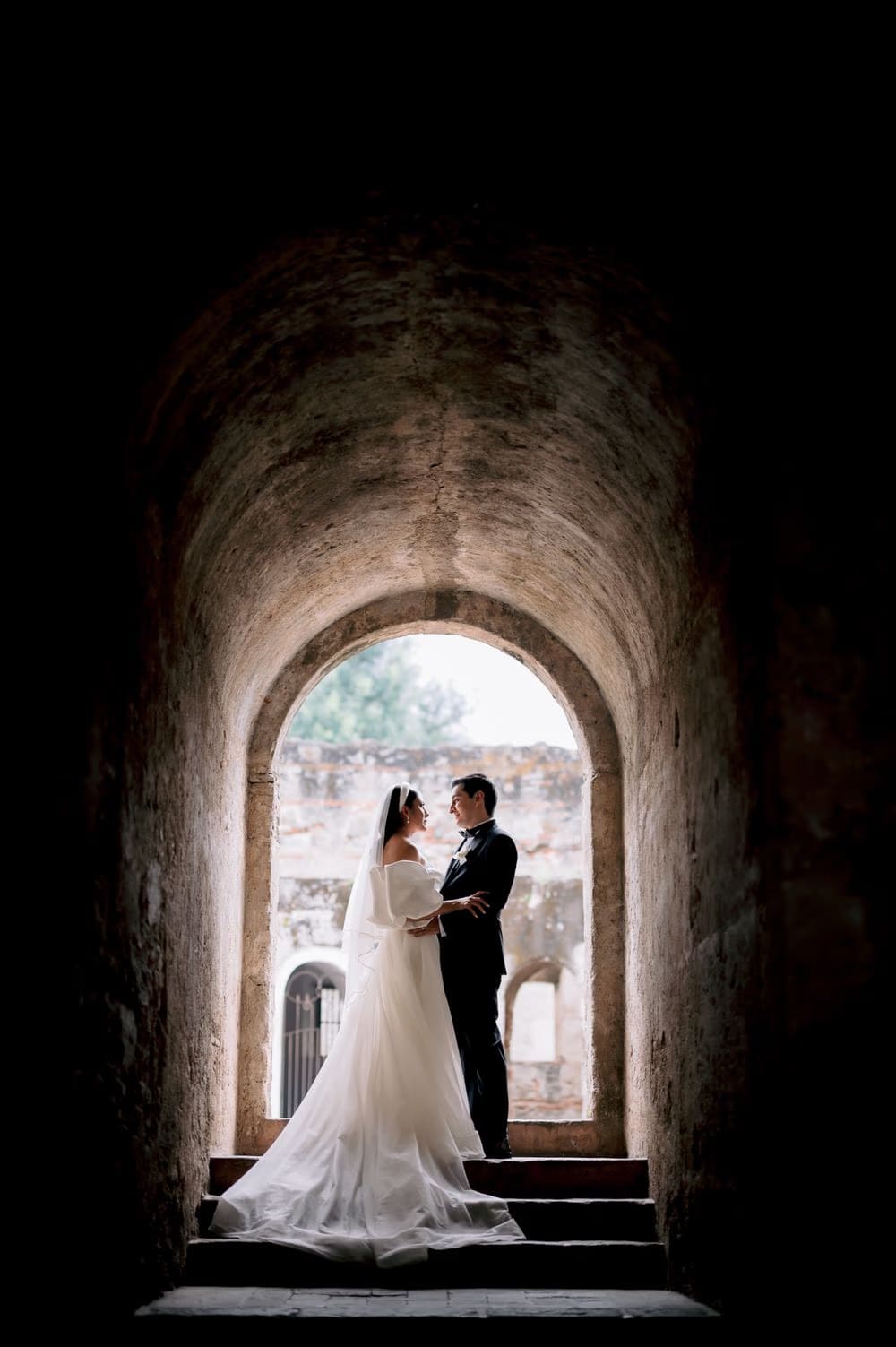 Bride and groom embrace in silhouette inside a vaulted brick passage of Capuchinas Ruins — black-and-white frame.