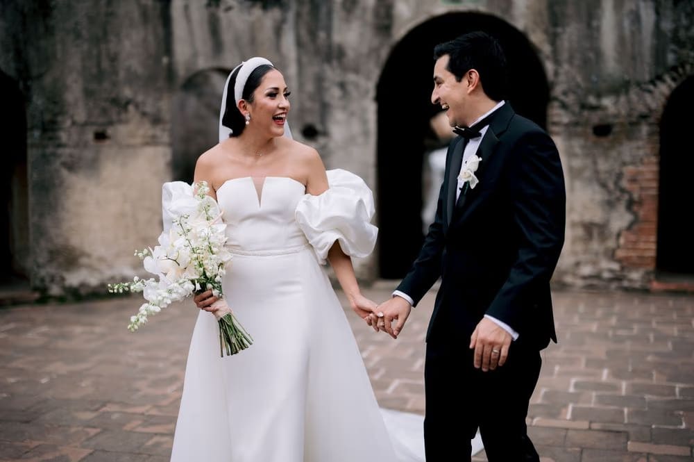 Bride and groom laugh holding hands in a courtyard of the convent — joyful candid frame.