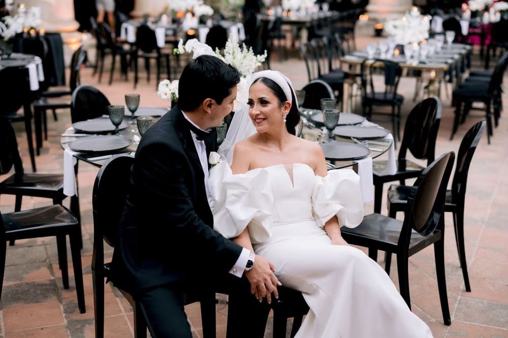 Bride and groom sit close at a reception table surrounded by candle-lit place settings.