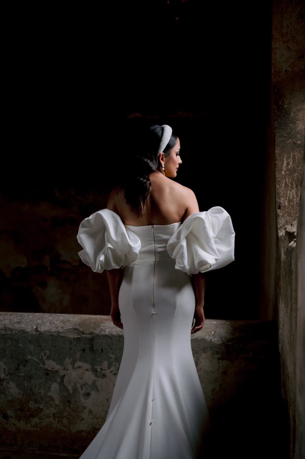 Back view of the bride in a fitted mermaid gown revealing the dramatic puff sleeves and button-back train.