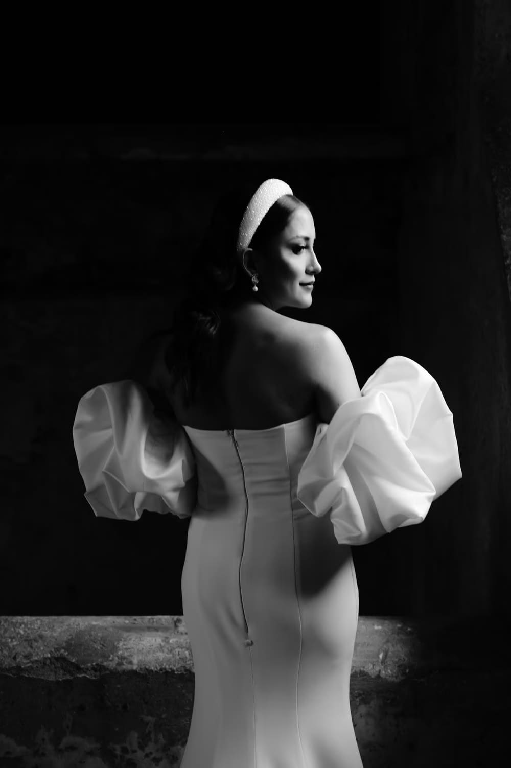 Bride looks back over her shoulder — black-and-white editorial showcasing puff sleeves and beaded headband.