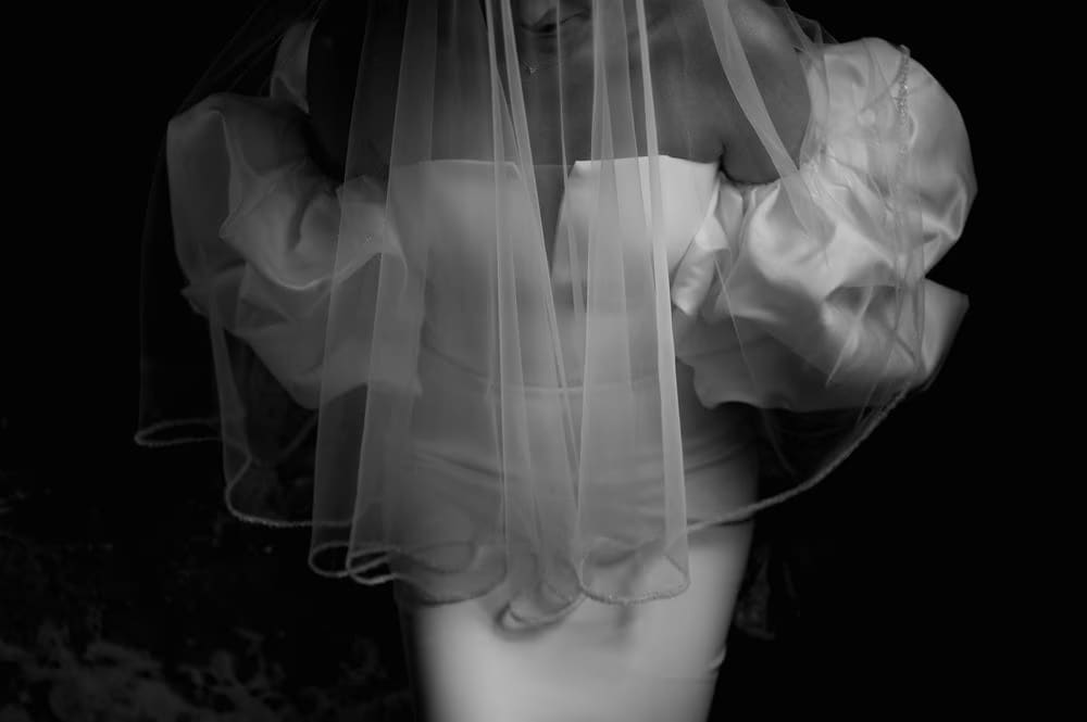 Abstract close-up of the bride's puff sleeves through a translucent veil — black-and-white art frame.