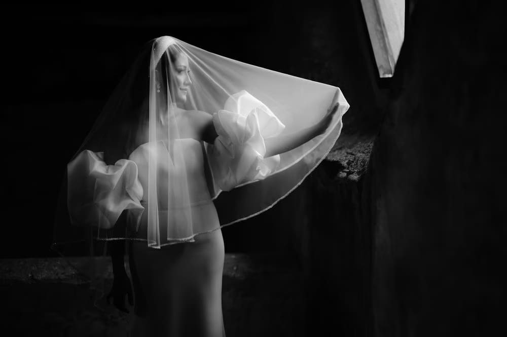 Bride twirls her veil to one side in dramatic motion — black-and-white editorial wedding frame.