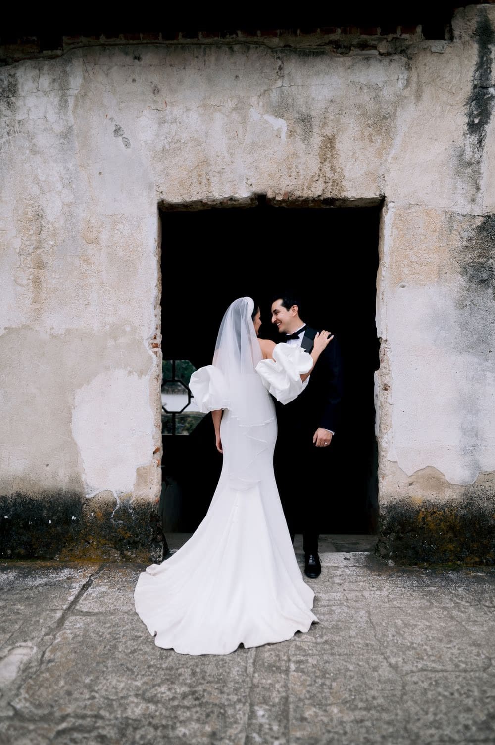 Bride and groom embrace in a weathered colonial doorway in Antigua Guatemala — destination wedding portrait.