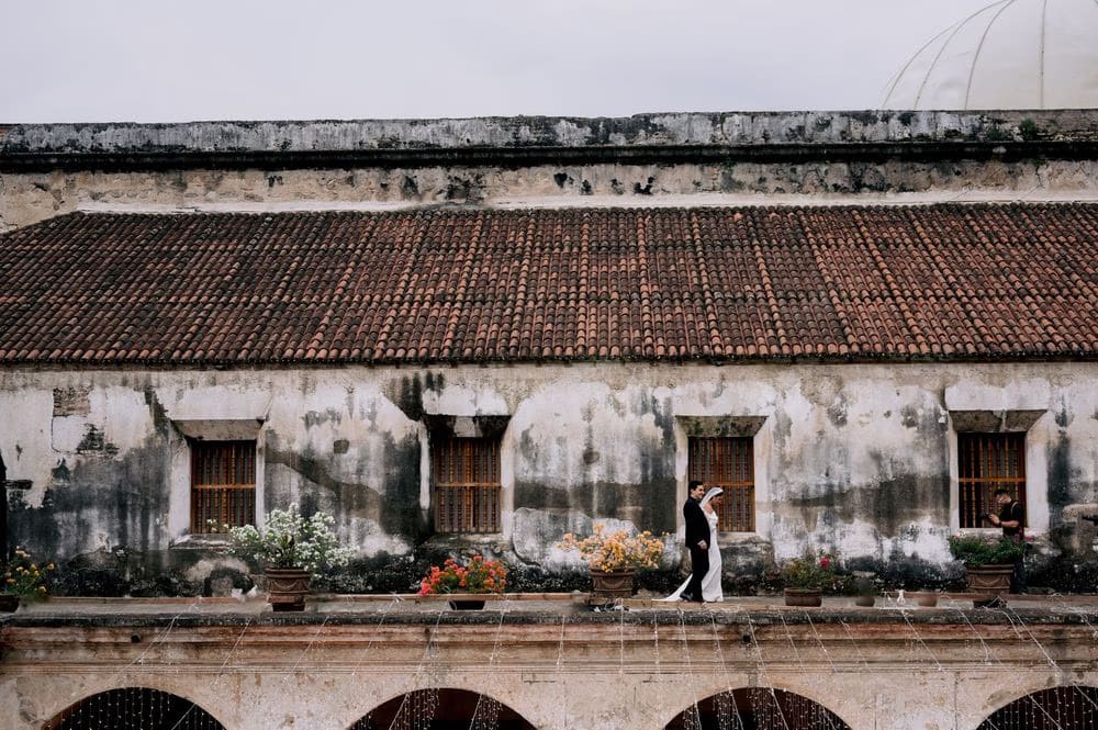 Wide environmental shot of the couple walking along the rooftop terrace of the convent ruins.