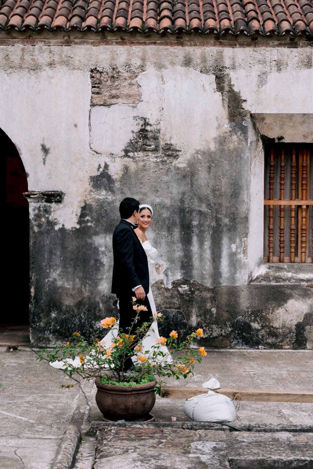Couple poses in front of a weathered colonial wall with a planted bougainvillea — Antigua editorial frame.